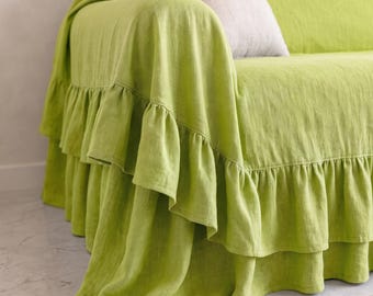May include: A lime green sofa cover featuring a double-layered ruffled skirt along the bottom edge. The fabric has a visible woven texture and is draped over the arm and base of a sofa, accompanied by a single light beige throw pillow.