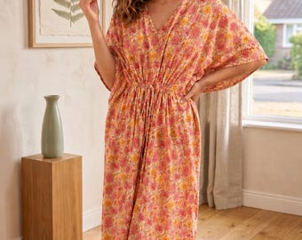 May include: A floor-length kaftan dress featuring a vibrant floral pattern in shades of pink, orange, and yellow. The garment has a V-neckline, wide short sleeves, and a drawstring waist tie that gathers the fabric to create a defined silhouette.
