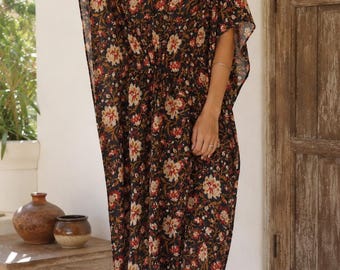 Puede incluir: Un vestido caftán largo hasta el suelo con una base negra y un estampado floral en tonos rojo, crema y verde. La prenda presenta un escote en V profundo, mangas cortas holgadas y un detalle de cintura ceñida con una silueta relajada.