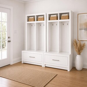 May include: Two white wooden storage units with drawers, hooks, and upper compartments. Each unit has a drawer with a silver handle, hooks for hanging items, and compartments holding woven baskets with folded towels.