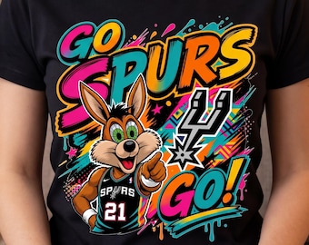 May include: Black t-shirt featuring a cartoon jackrabbit wearing a basketball jersey with the number 21. The shirt has the words "GO SPURS GO!" in colorful, graffiti-style lettering, along with the Spurs team logo.
