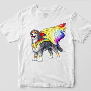 May include: White t-shirt with a cartoon dog in a superhero costume. The dog has a rainbow-colored cape, mask, and armbands. The dog is grey and white with a star emblem on its chest.