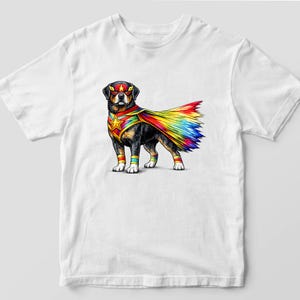 May include: White t-shirt featuring a Rottweiler dog dressed as a superhero. The dog wears a red mask, a star-shaped chest emblem, and a colorful cape with rainbow hues. The dog also has matching arm and leg bands.
