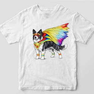 May include: White t-shirt featuring a superhero dog illustration. The dog is black and white with a rainbow cape, mask, and armbands. A gold star is on the dog's chest. The design is a colorful and whimsical depiction of a canine superhero.