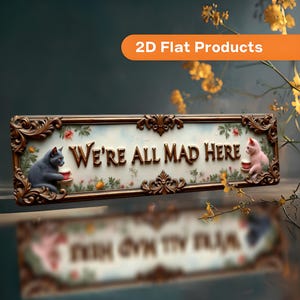 May include: A rectangular wall sign with an ornate bronze-colored frame featuring the text "WE'RE ALL MAD HERE" in raised lettering. The sign displays a grey cat on the left and a pink cat on the right, both holding small cups amidst floral accents.