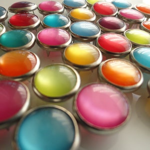 May include: Assortment of colorful round buttons with a metallic finish. The buttons are arranged in a random pattern and have a variety of colors, including blue, green, red, yellow, orange, and pink.