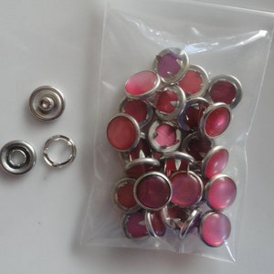 May include: A bag of pink snap buttons with silver metal settings. The buttons are in a clear plastic bag.