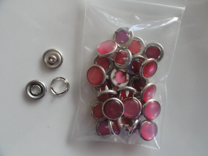 May include: A bag of pink snap buttons with silver metal settings. The buttons are in a clear plastic bag.