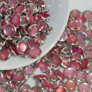 May include: A large pile of pink and silver decorative nailheads. The nailheads have a round, slightly domed top and a silver base with four prongs.