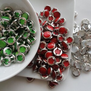 May include: A close-up of three bowls of colorful buttons. The bowls are white and the buttons are silver with green, red, and clear centers.