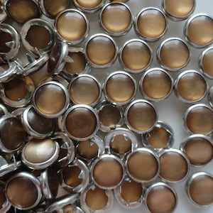 May include: A pile of brown and silver round buttons with a raised center. The buttons have a shiny finish and are perfect for adding a touch of elegance to any project.