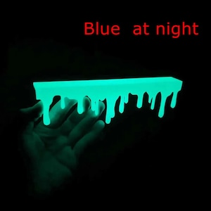 Pu&ograve; includere: Un oggetto rettangolare fluorescente con un design a goccia di colore turchese brillante. Il testo rosso "Blue at night" &egrave; presente. L'oggetto &egrave; su sfondo nero.