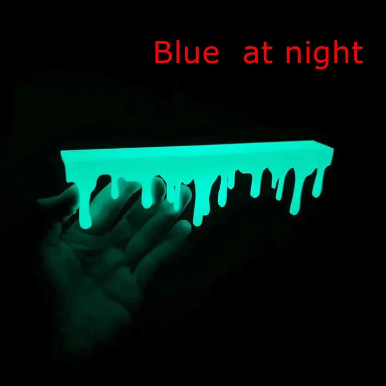 Pu&ograve; includere: Un oggetto rettangolare fluorescente con un design a goccia di colore turchese brillante. Il testo rosso "Blue at night" &egrave; presente. L'oggetto &egrave; su sfondo nero.