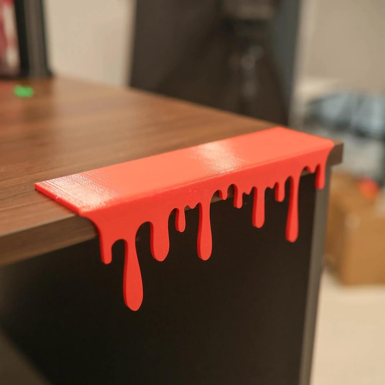 Pu&ograve; includere: Un bordo per scrivania rosso brillante con un design a goccia di vernice. Il pezzo rettangolare &egrave; realizzato in un materiale solido ed &egrave; progettato per adattarsi al bordo di una scrivania o di un tavolo. Un accessorio decorativo unico e accattivante.