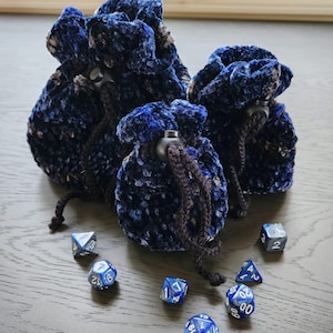 May include: Three blue and black velvet drawstring bags with a black cord and a black toggle. The bags are filled with blue and silver dice.