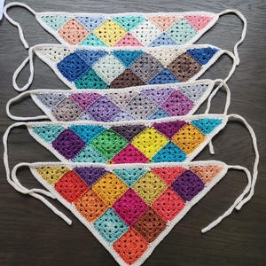 May include: Five colorful, handmade crochet bandanas. Each bandana features a granny square design in a variety of colors, including pink, blue, green, yellow, and purple. The bandanas have white borders and ties.
