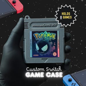 May include: A grey plastic game cartridge case shaped like a classic Nintendo Game Boy cartridge. The label features a purple Gastly Pokémon graphic with the text Pokémon. A starburst graphic states HOLDS 8 GAMES. Text below reads Custom Switch GAME CASE.