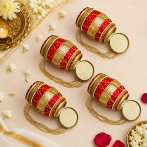 May include: Four cylindrical red fabric containers with gold metallic trim and white polka dots. Each container features a gold-toned lid and a delicate gold chain attached to the base, arranged in a diagonal pattern on a light surface.