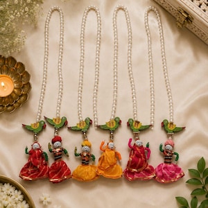 May include: Six decorative wall hangings featuring white pearl bead strands, each topped with a small green parrot figure and finished with a miniature fabric doll wearing a colorful outfit in red, yellow, orange, pink, and striped patterns.