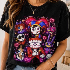 May include: A black t-shirt featuring a vibrant graphic print of various cartoon characters, including a jester, a figure with large teeth, a purple rabbit, and a doll, surrounded by glowing pink hearts and yellow stars against a dark background.