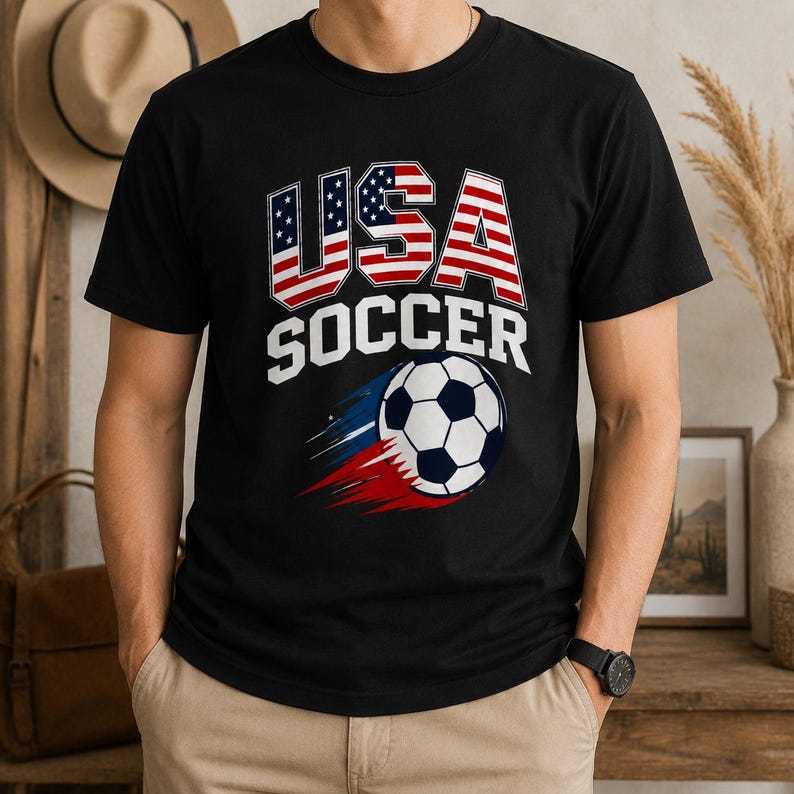 May include: Black t-shirt with "USA SOCCER" text and a soccer ball graphic. The text "USA" is designed with the American flag. The soccer ball has a blue, white, and red trail.