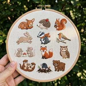 Könnte beinhalten: Gesticktes Waldtier-Hoop-Art mit einem Reh, Igel, Eichhörnchen, Kaninchen, Dachs, Rotkehlchen, Mäusen, Fuchs, Eule, Ottern, Maulwurf und Bär. Die Tiere sind in verschiedenen Braun-, Orange- und Grautönen auf cremefarbenem Stoff.