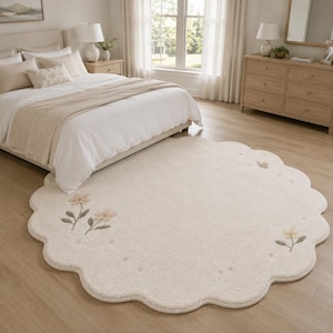 Könnte beinhalten: Ein großer, runder, cremefarbener Teppich mit gewelltem Rand. Der Teppich ist mit gestickten Blumenmotiven in sanften Pastelltönen wie Rosa, Gelb und Grün sowie kleinen, über die Oberfläche verteilten Schmetterlingsstickereien verziert.