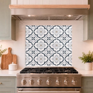 May include: A square kitchen backsplash panel featuring a repeating geometric pattern in shades of charcoal grey, light grey, and white. The design consists of interconnected quatrefoil shapes with central floral motifs, installed behind a stainless steel stove.