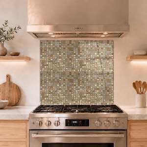 Könnte beinhalten: Eine quadratische Küchenrückwand mit einem Gitter aus kleinen, reflektierenden Mosaikfliesen in verschiedenen Metallic-Tönen wie Gold, Bronze und Silber. Die Fliesen bilden eine strukturierte, schimmernde Oberfläche hinter einem Gasherd.