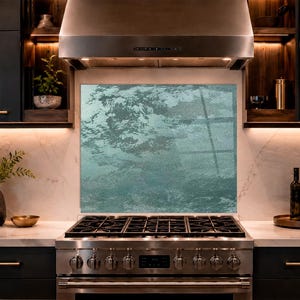 May include: A rectangular kitchen backsplash panel featuring a textured, abstract design in shades of teal and seafoam green. The panel is positioned behind a stainless steel gas range and stove, set against a light-colored marble wall surface.