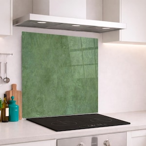 Puede incluir: Un panel protector de cocina rectangular con un acabado texturizado en color verde salvia y un sutil patrón moteado. El panel está colocado verticalmente detrás de una placa de inducción negra, sirviendo como protección para la pared.