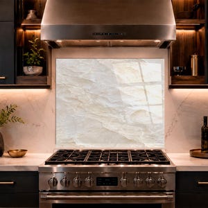 Peut inclure: Un panneau de crédence de cuisine rectangulaire présentant un motif de pierre de marbre beige clair et crème avec des veines subtiles. Le panneau est positionné verticalement derrière une cuisinière à gaz en acier inoxydable.