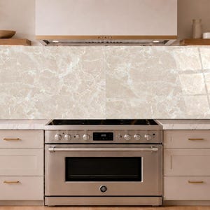 Peut inclure: Un panneau de crédence de cuisine rectangulaire présentant un motif en marbre beige clair brillant avec des veines blanches. Le panneau est installé horizontalement derrière une cuisinière en acier inoxydable, offrant une surface lisse et réfléchissante.