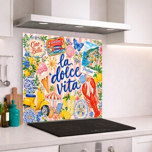 Op de afbeelding: Een rechthoekig keukenachterwandpaneel met een kleurrijke collage van Italiaans getinte illustraties, waaronder een gele scooter, een kreeft, een ijshoorntje en de tekst "Ciao Bella" en "la dolce vita" op een roze gestreepte achtergrond.
