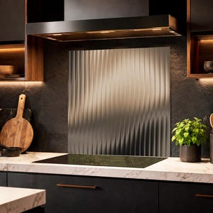 May include: A rectangular metallic kitchen backsplash panel featuring a vertical fluted or ribbed texture. The panel is installed on a dark stone wall behind a black induction cooktop, positioned between dark cabinetry and under a range hood.