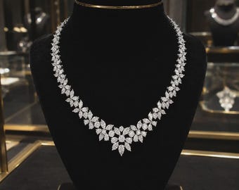 May include: A silver-toned necklace featuring a continuous arrangement of marquise and pear-cut clear stones. The design showcases a floral-inspired pattern that tapers toward the center, creating a symmetrical, vine-like structure of faceted gems.