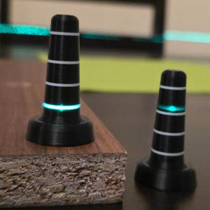 May include: Two black, cone-shaped objects with white stripes and a glowing green band. The objects are on a wooden surface. The objects appear to be small, possibly decorative or functional.
