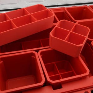 Puede incluir: Contenedores de almacenamiento de plástico rojo con múltiples compartimentos. Los contenedores están diseñados para encajar dentro de una caja más grande, ofreciendo soluciones de almacenamiento organizadas. La imagen muestra varios tamaños y configuraciones de los compartimentos.