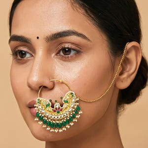 Pode incluir: Um piercing de nariz dourado com um pendente ornamentado. O pendente apresenta pedras preciosas verdes e vermelhas, pérolas brancas e detalhes dourados intrincados. Uma corrente delicada estende-se até à orelha. Joia para o nariz.