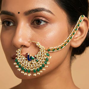 May include: An elaborate gold-coloured nose ring with a peacock motif, incorporating blue and green enamel, and hanging green and white beads. The piece is connected to the ear with a chain of green and white beads. This is a traditional Indian nose accessory.