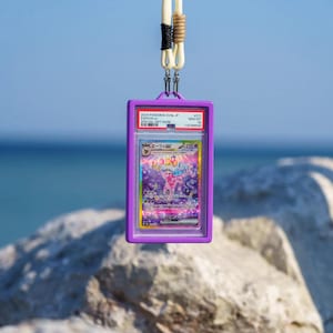 May include: A graded 2024 Pokemon Espeon ex trading card encased in a purple plastic holder, suspended by a cream-colored cord with black and tan accents. The card features Japanese text and a holographic illustration of the character Espeon.