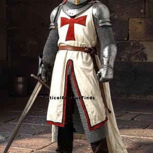 Könnte beinhalten: Eine Rüstung mit einem silbernen Helm mit goldenem Kreuz, einem weißen Überwurf mit rotem Kreuz, Kettenhemdärmeln, Schulter- und Handschutz aus Metall, einem braunen Ledergürtel und braunen Stiefeln. Ein Schwert wird gehalten. Text: NauticalArmourFinds.