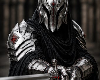 May include: A suit of silver metal armor featuring a spiked helmet with red accents, layered shoulder pauldrons with red gems, and articulated gauntlets holding a sword. The armor is worn over a textured black fabric cloak with visible text.