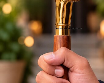 May include: A walking stick featuring a polished gold-colored metal handle shaped like a dog head with long ears. The shaft is made of smooth, brown wood with a visible grain. The text NauticalArmourFinds is printed on the metal collar.