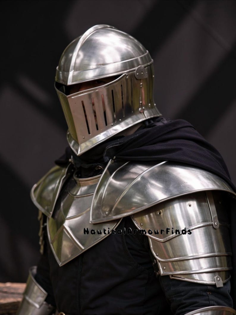 May include: A polished silver knight's helmet and shoulder armor. The helmet features a visor with vertical slits and a rounded top. The shoulder armor is layered and reflective, with the text "Nautical Armour Finds" visible.