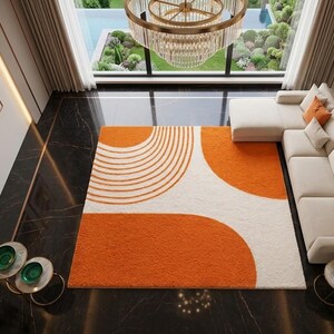 May include: A rectangular area rug featuring a high-pile texture with a white base and bold orange geometric patterns, including a series of concentric semi-circles and large solid curved shapes, positioned in a room with dark marble flooring.