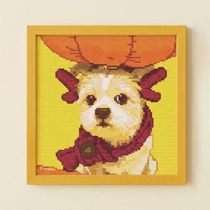 Puede incluir: Una obra de arte de punto de cruz de un perro con un sombrero de calabaza y una bufanda burdeos. El perro tiene pelaje blanco y canela, con ojos oscuros y una nariz marrón. El fondo es amarillo y la obra está enmarcada en un marco de madera amarillo.