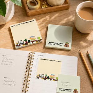 May include: Two square sticky note pads with illustrations. One is cream-colored with the text "HERE'S A NOTE TO CLUTTER YOUR DESK" and a desk graphic. The other is light green with the text "I'M ONLY HERE UNTIL I WIN THE LOTTERY" and a money bag.