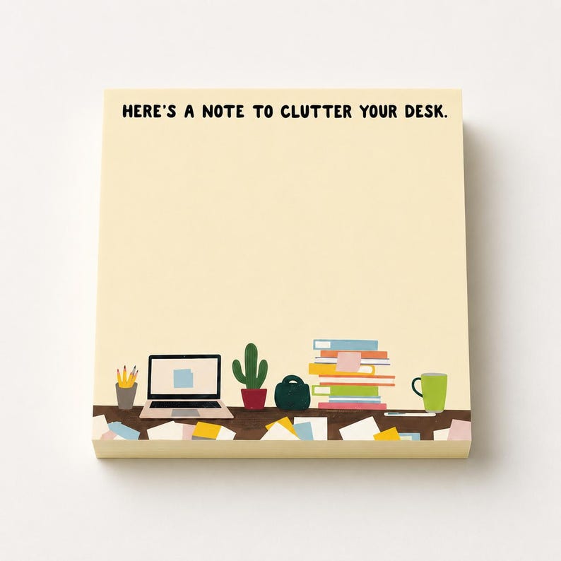 May include: A square notepad with a light cream background featuring the black text HERE'S A NOTE TO CLUTTER YOUR DESK. The bottom section displays a colorful illustration of a desk with a laptop, a potted cactus, a stack of books, and a mug.