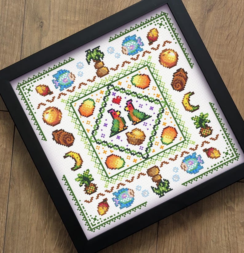 May include: Framed cross-stitch art featuring a tropical theme. The design includes parrots, mangoes, coconuts, pineapples, bananas, and fish. The artwork is framed in a black square frame and set against a light wood background.